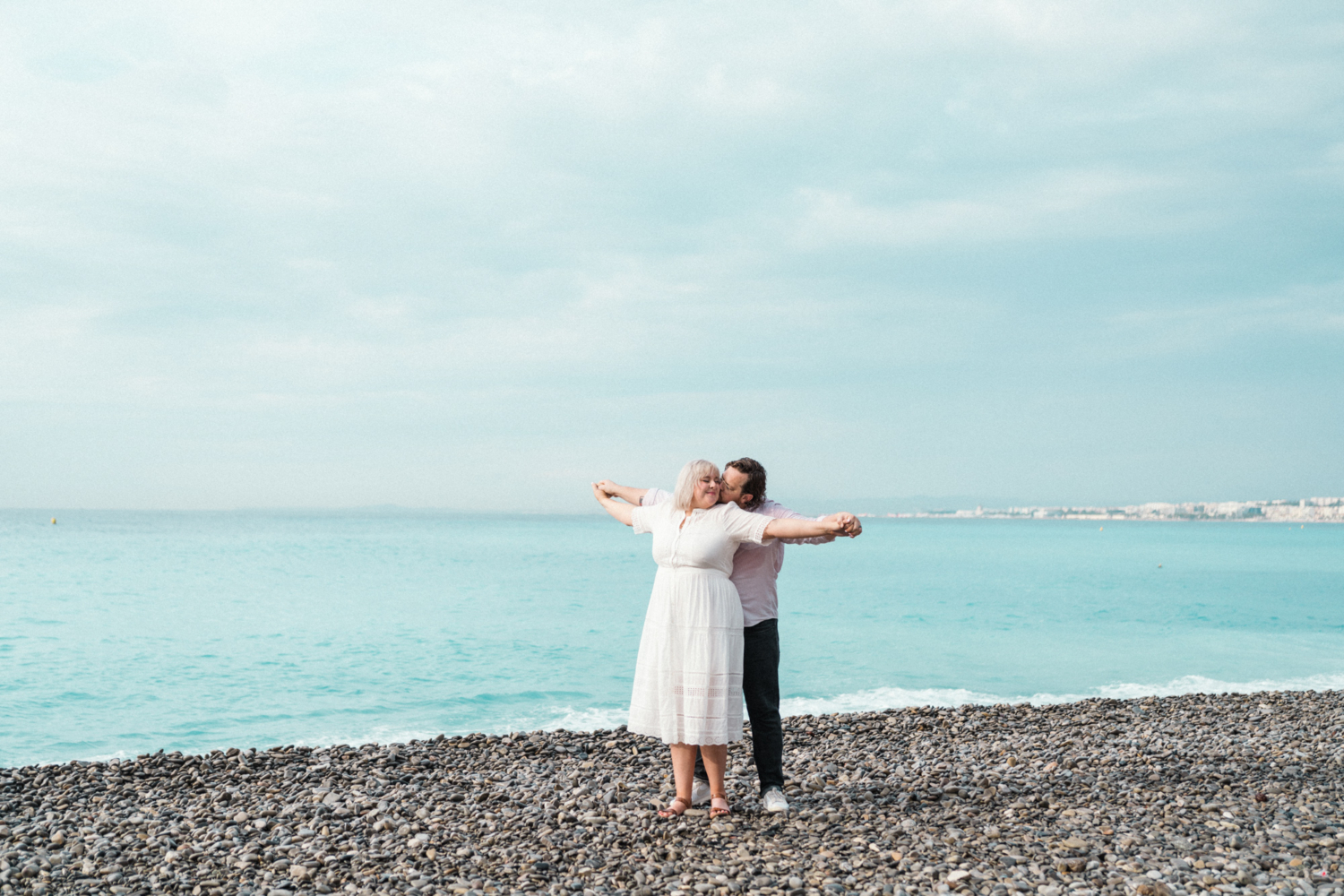 man kisses woman's cheek with sea in background