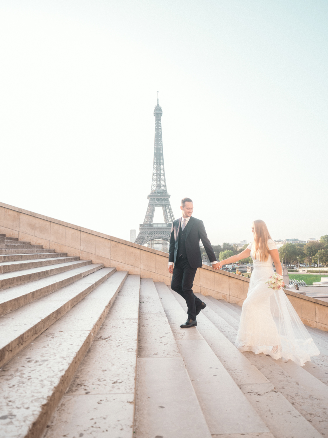 bride and groom walk up staircase with view of eiffel towe