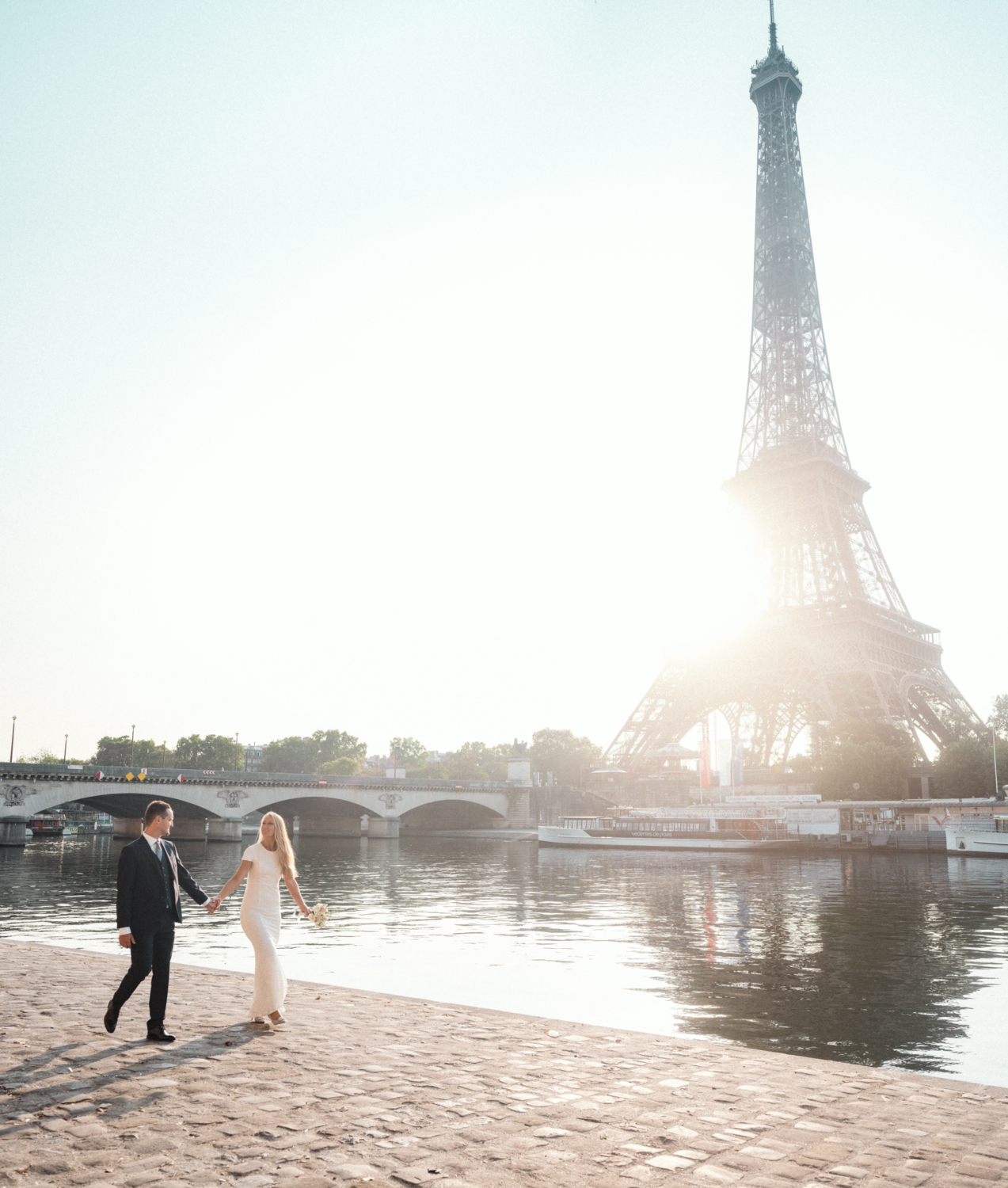 bride and groom walk along the seine river in paris
