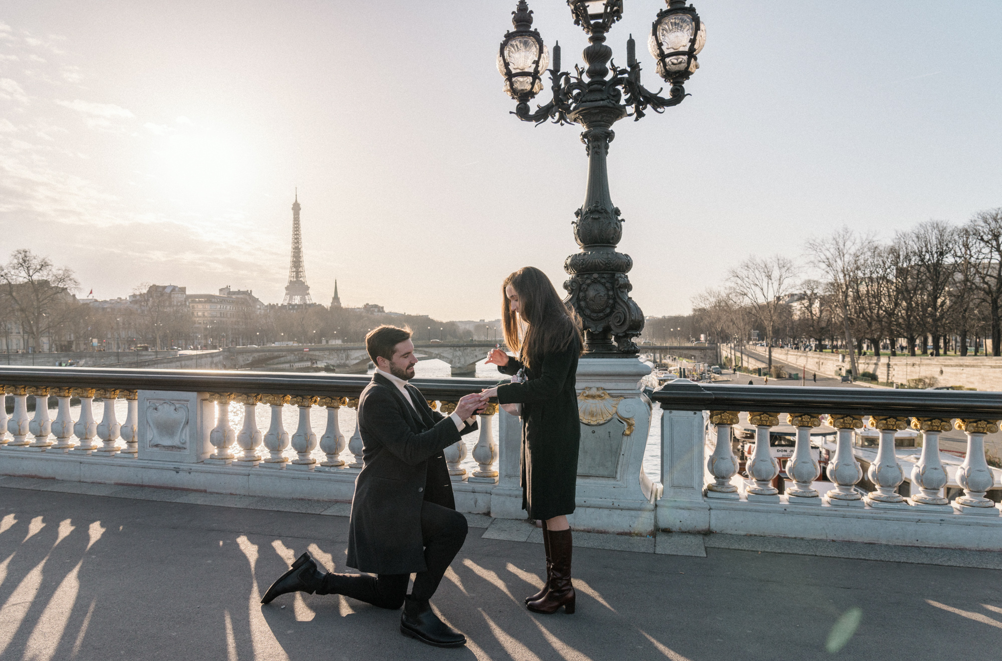 man places engagement ring on woman's hand on bridge in paris