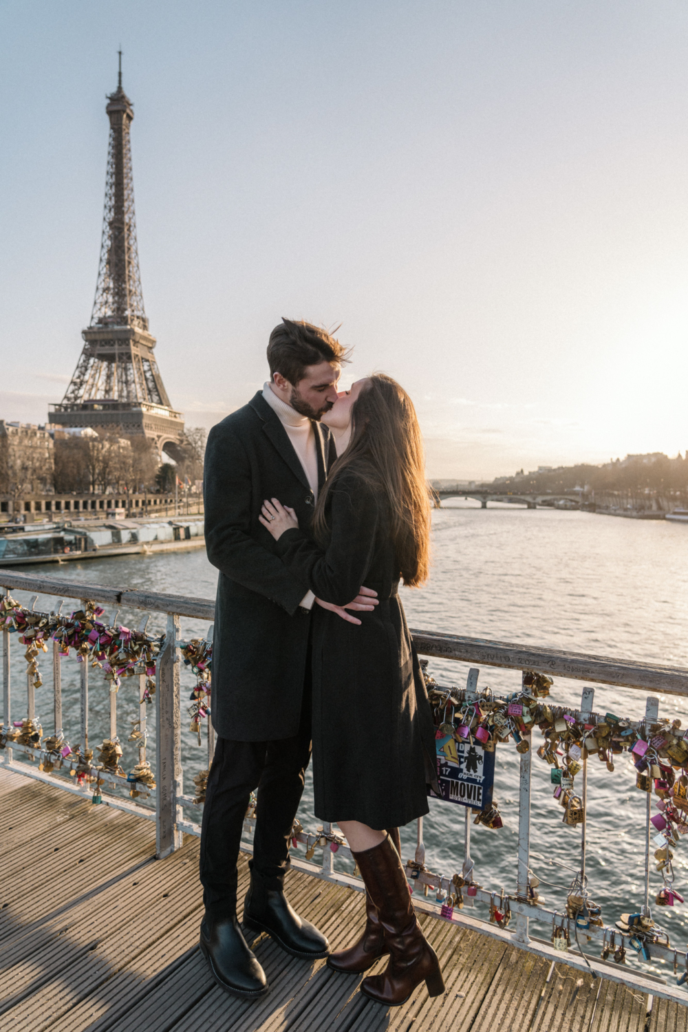 newly engaged couple kiss passionately on bridge with view of eiffel tower