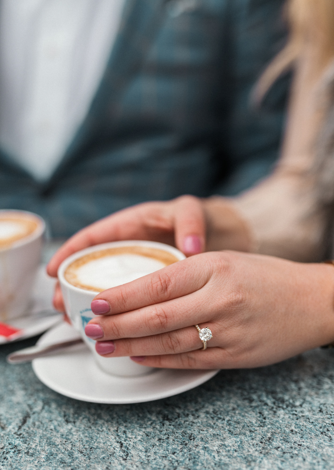 woman holds coffee cup showing off new diamond engagement ring in paris