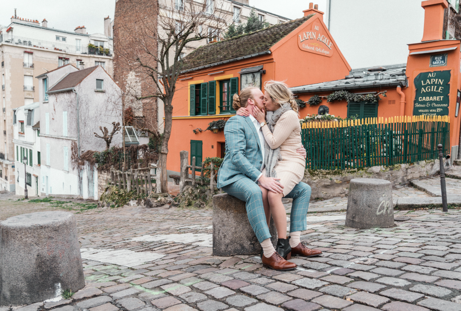 newly engaged couple passionately kiss in front of lapin agile in montmartre