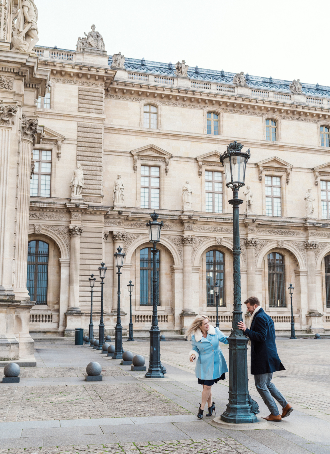 engaged couple run around a lamp at the louvre in paris