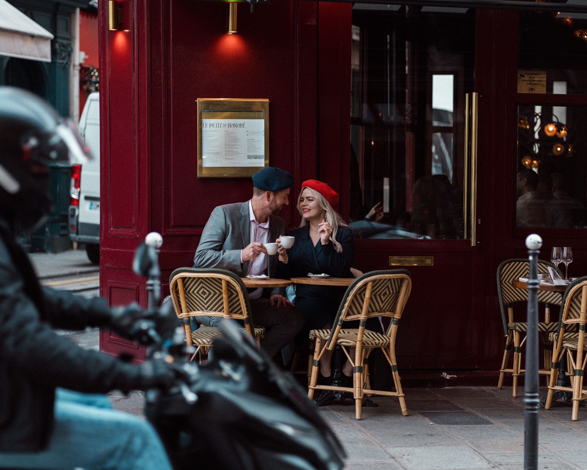 couple drinking coffee in paris with motorcycle passing