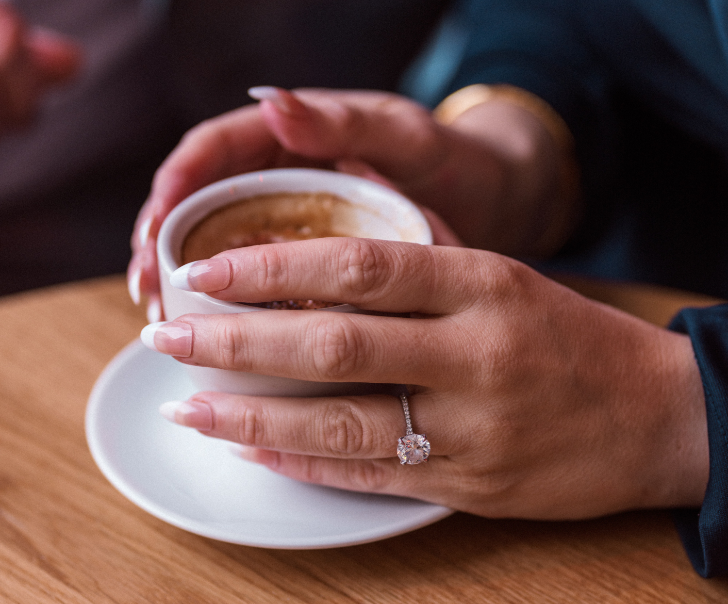woman holding cup of espresso with engagement ring