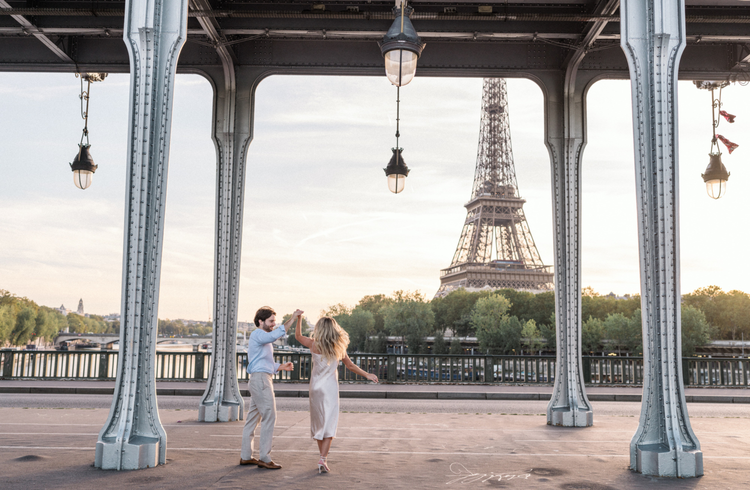 engaged couple dance under bridge with view of the eiffel tower in paris