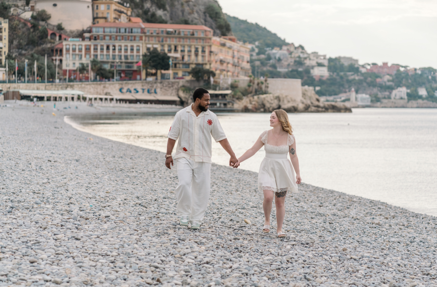 cute newlywed couple walk on pebble beach in nice france