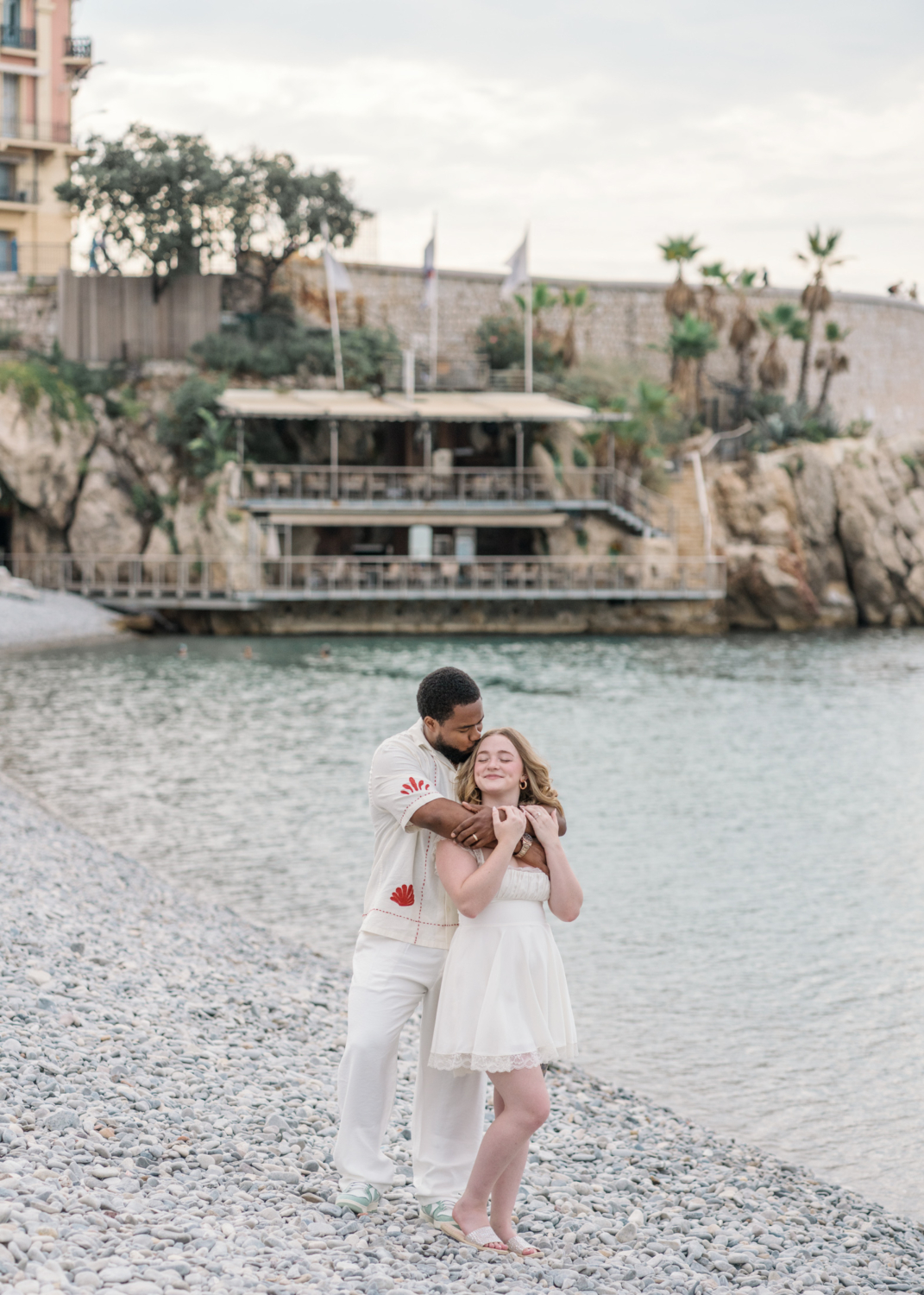 husband embraces wife on the rocky beach of nice france