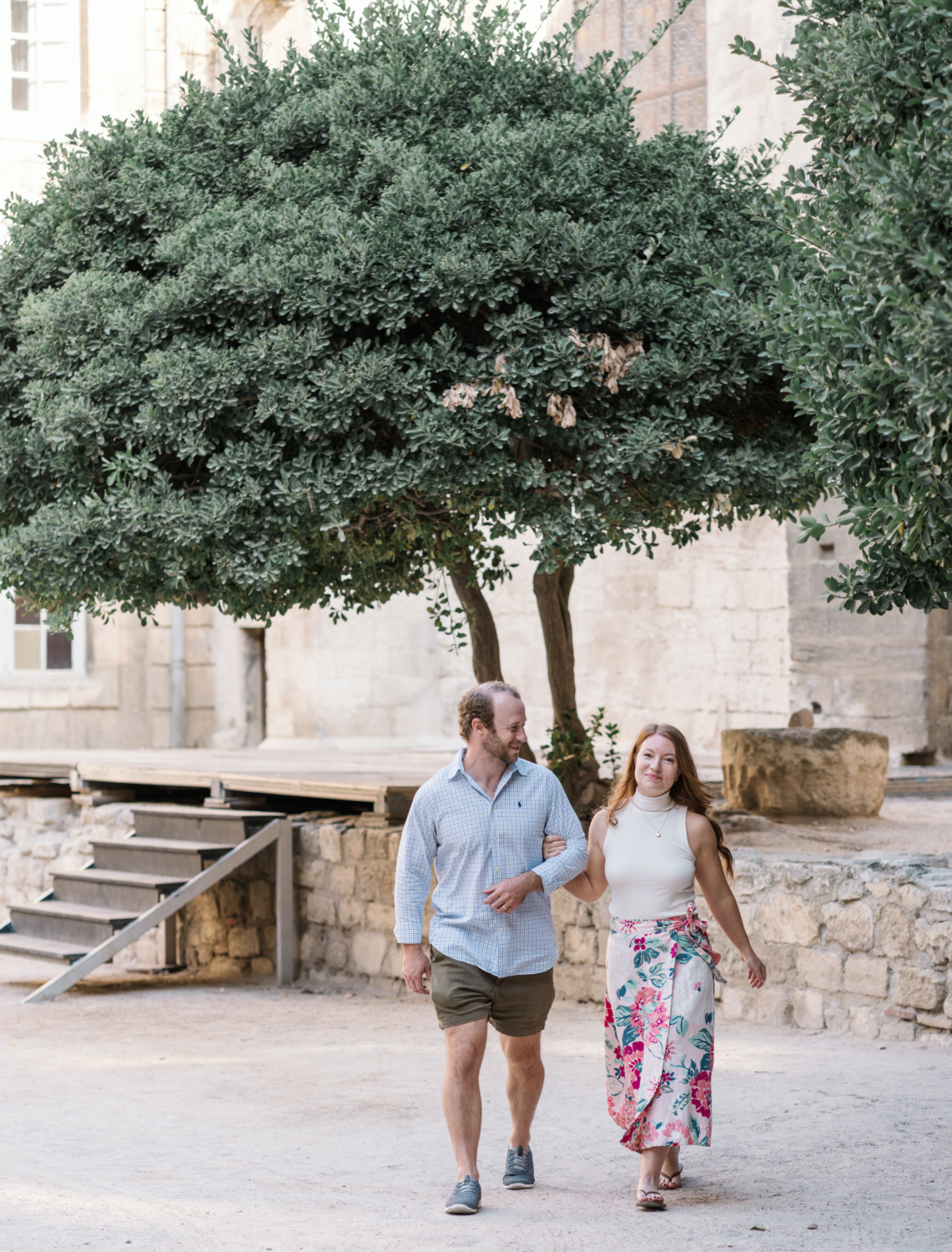 cute couple walk arm in arm next to beautiful tree in arles france