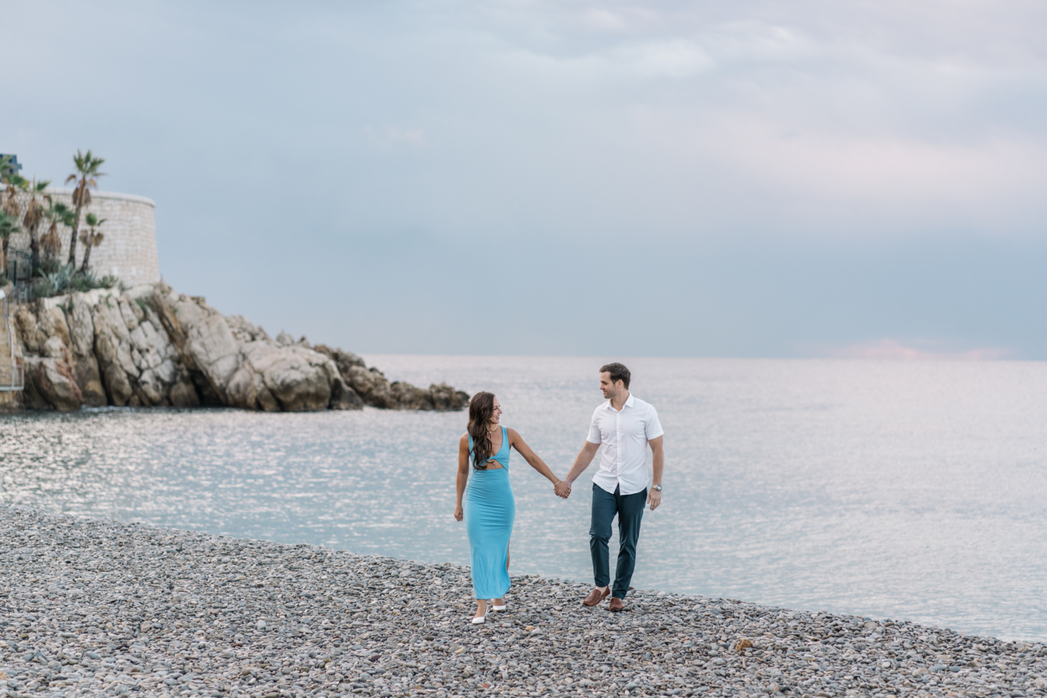 beautiful couple walk on stone beach with view of sea in nice france