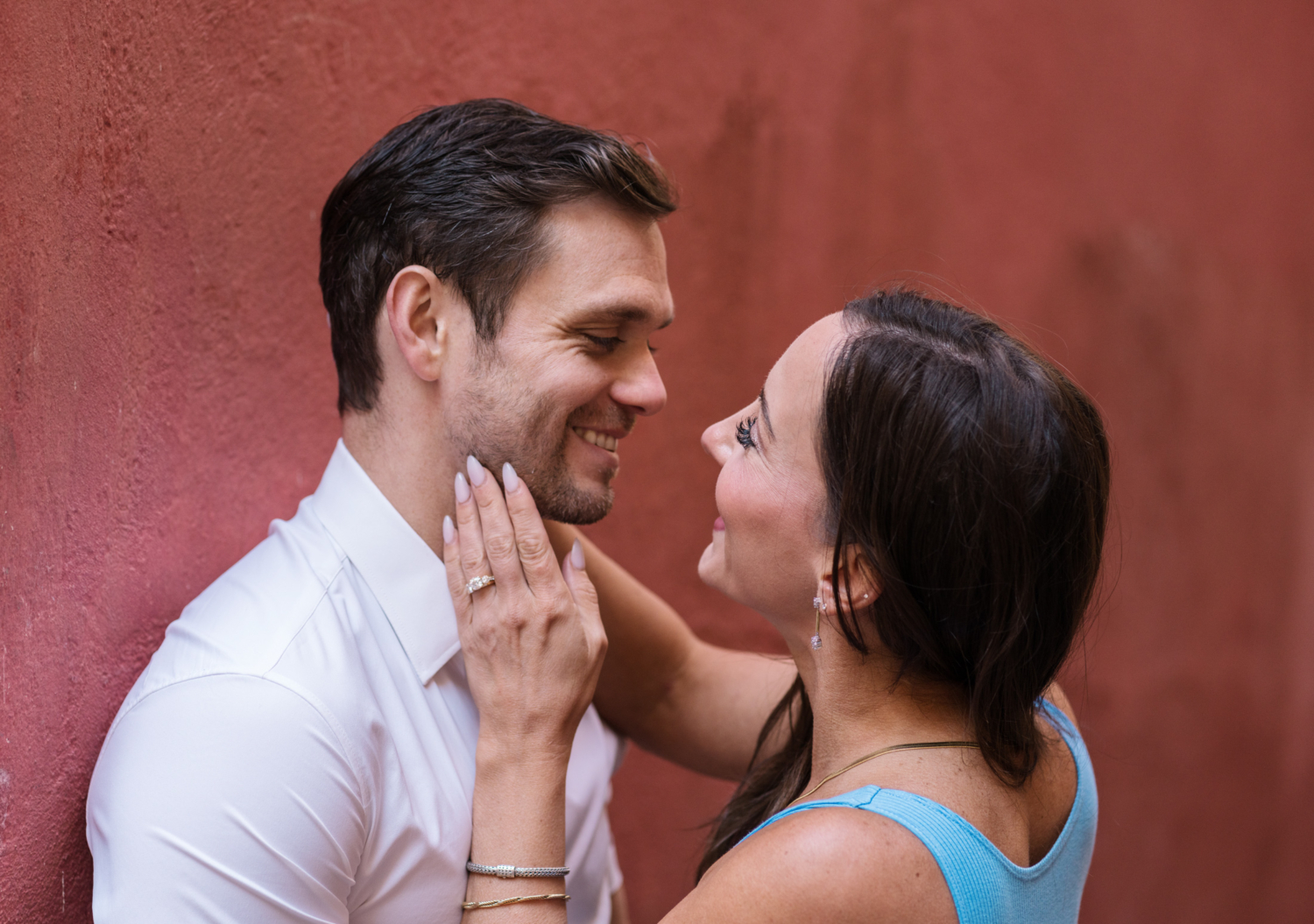 husband and wife smile at each other next to red wall in nice france