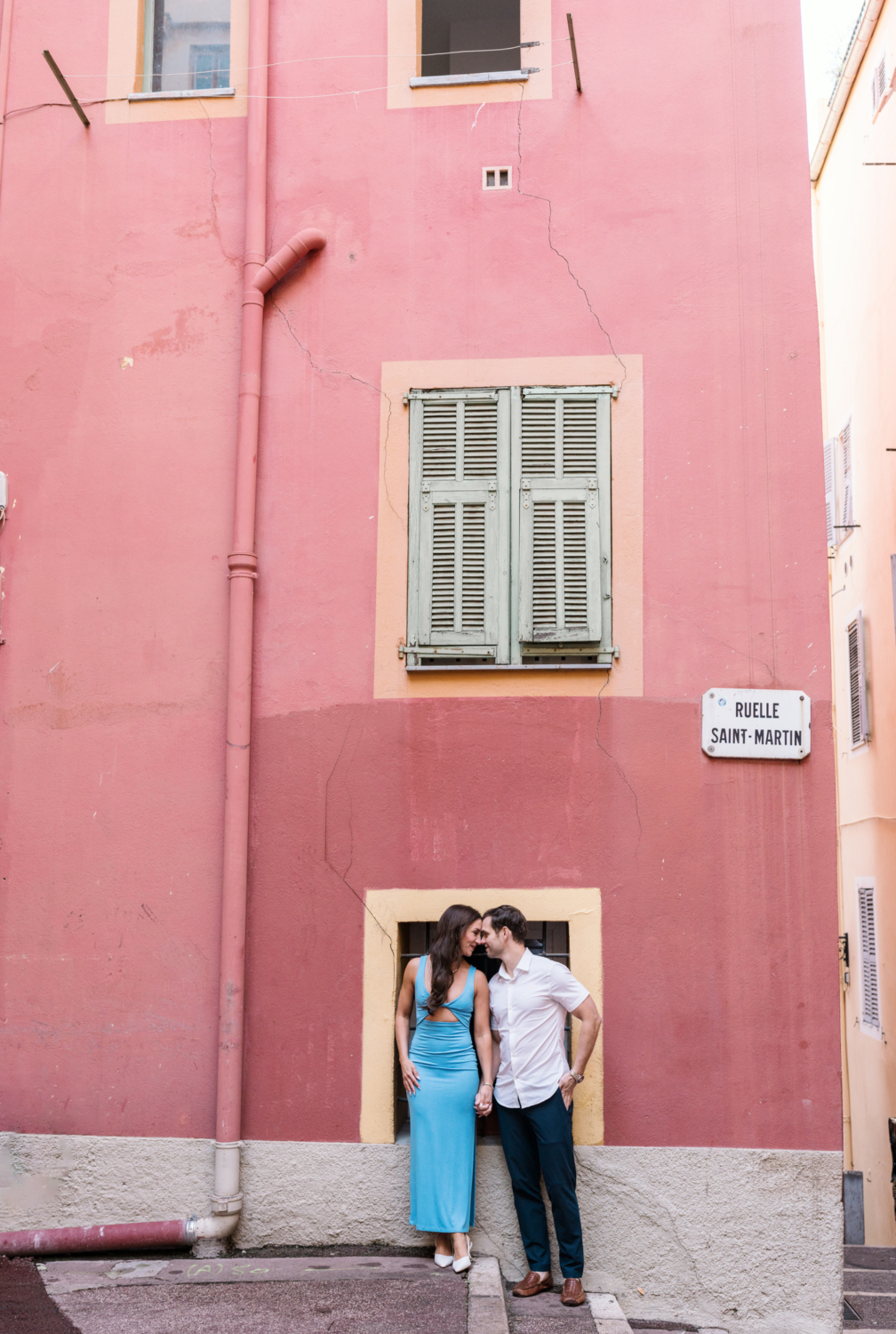 newlyweds pose in front of salmon colored building in nice france