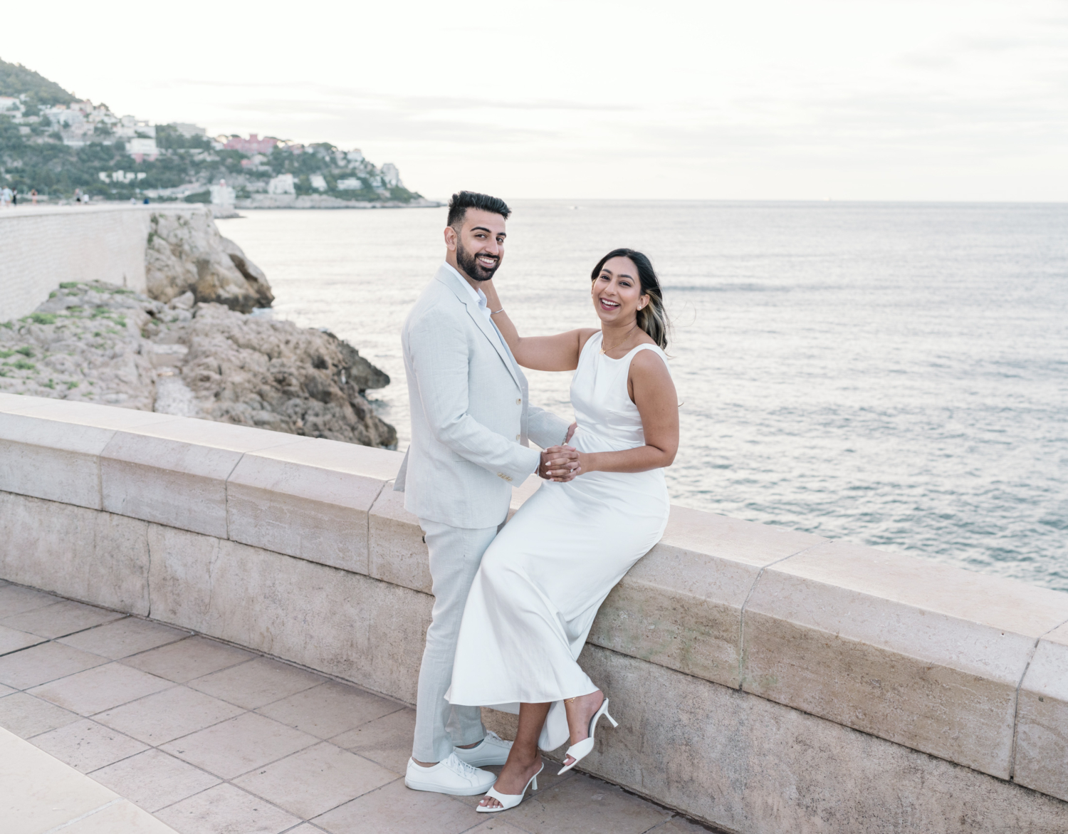 cute engaged couple laugh as they pose along boardwalk in nice france