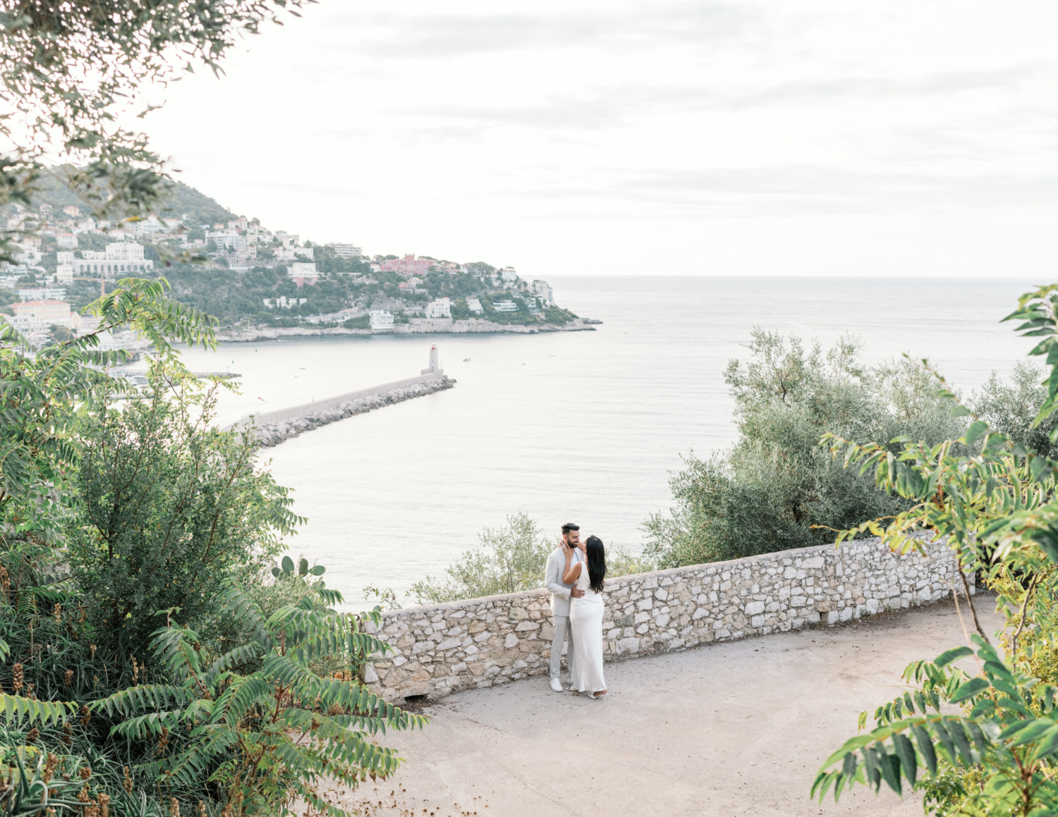 engaged indian american couple embrace with view of lighthouse in nice france