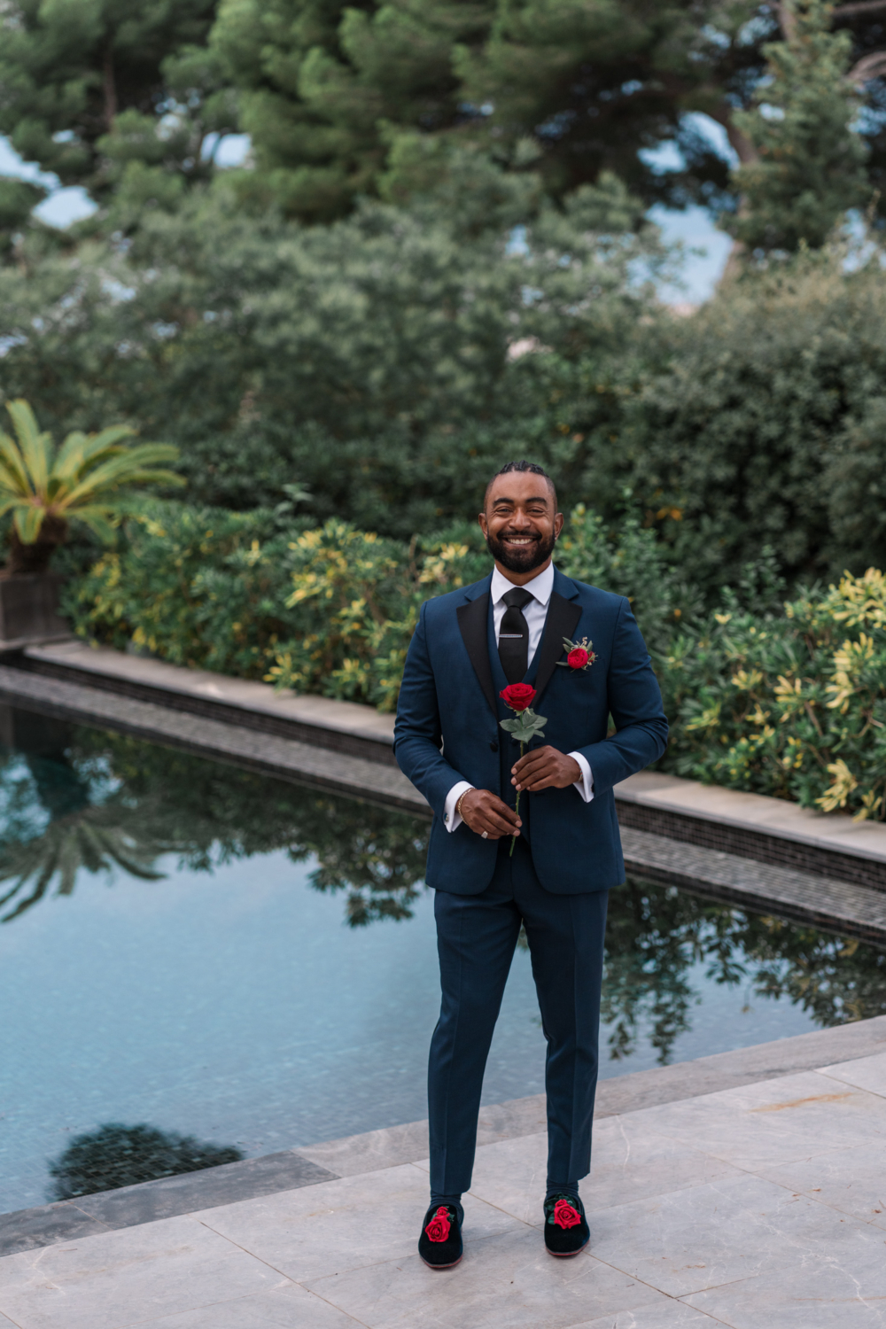 groom smiles and holds rose next to swimming pool in antibes france