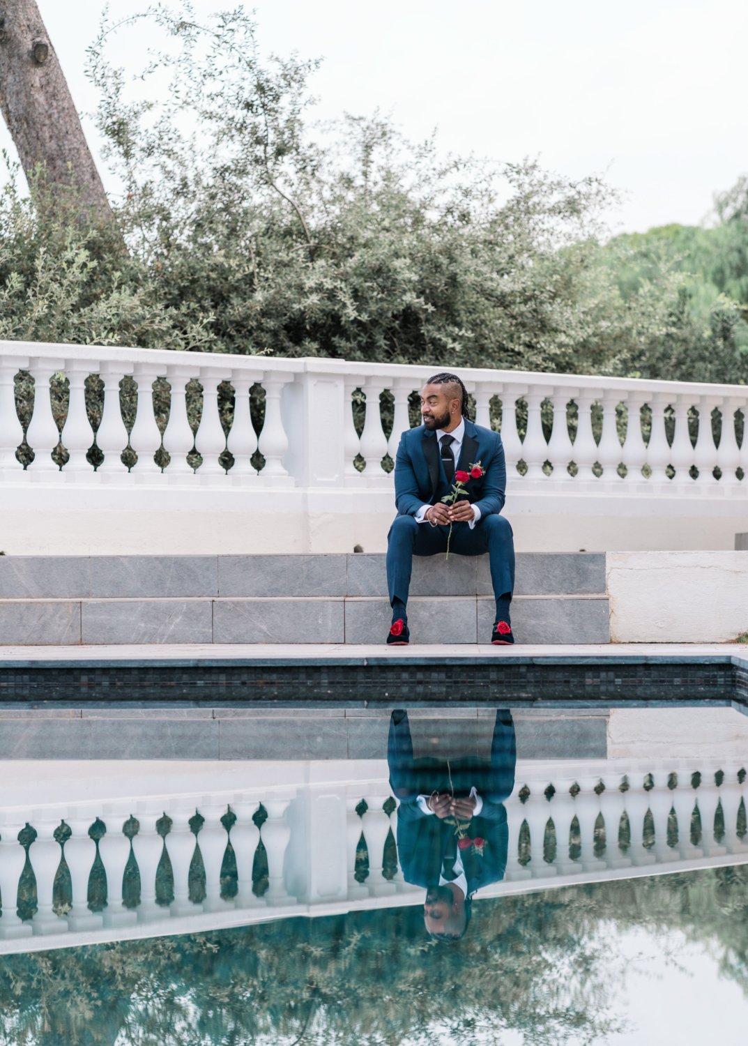 groom sits at pool with rose in his hand in antibes france