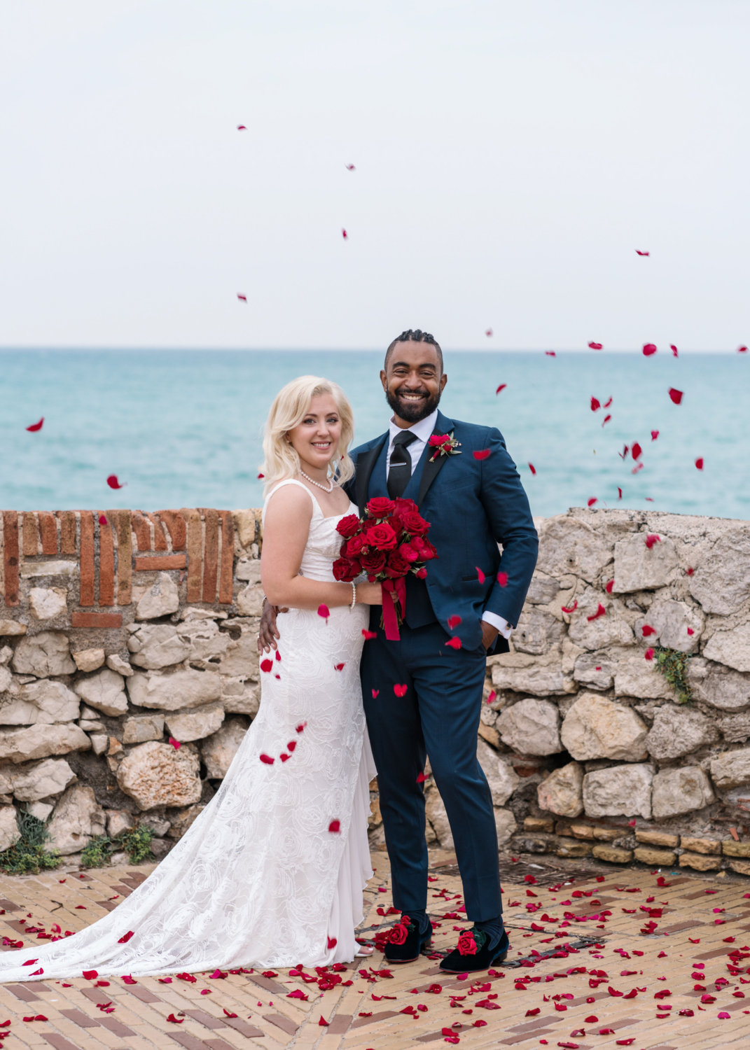 bride and groom pose with rose petals flying in air in antibes france