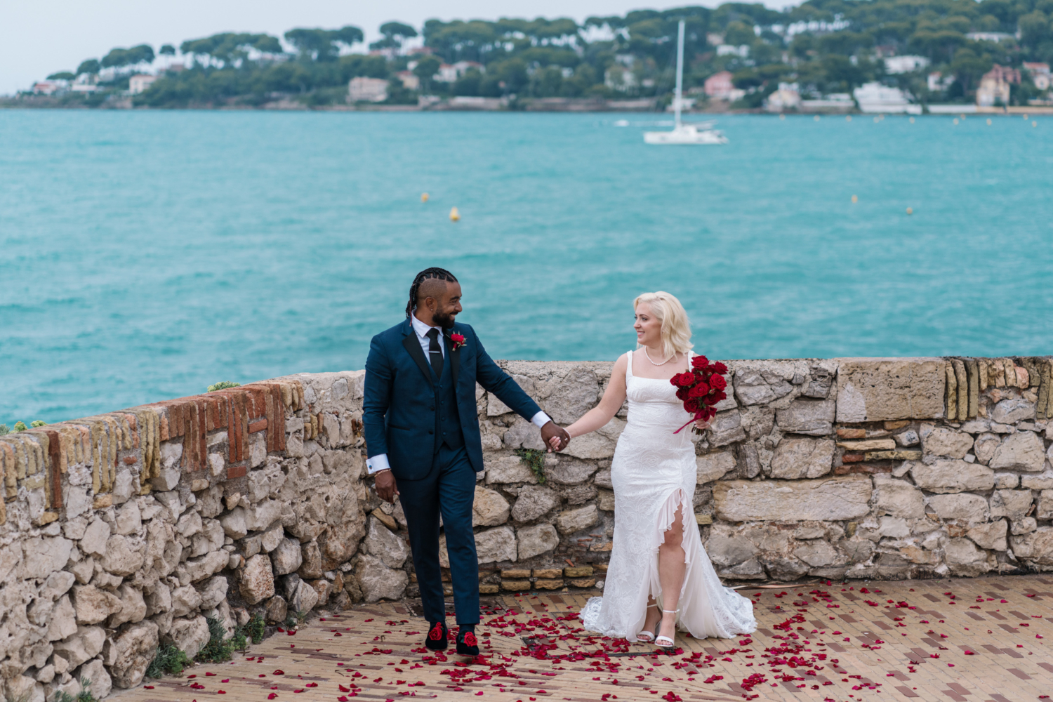 bride and groom walk and smile with view of sea in antibes france