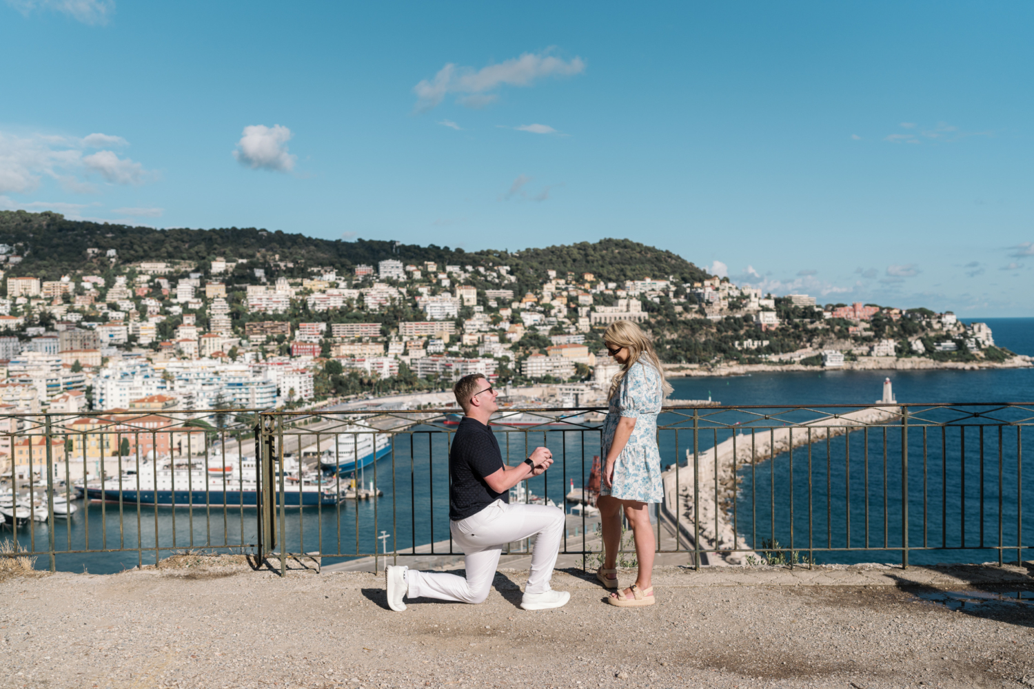 man on one knee presents ring to woman during their surprise proposal with view of sea in nice france