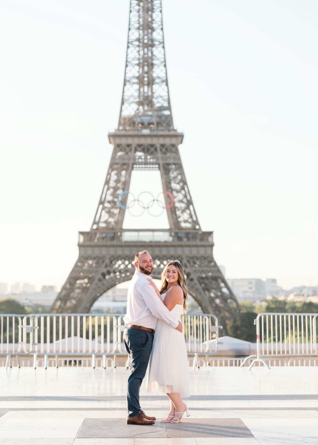 cute engaged couple pose in front of eiffel tower with olympic rings