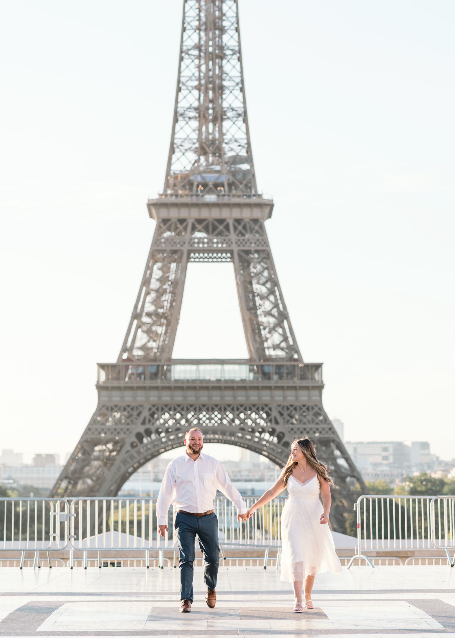 engaged couple laugh and walk in paris with view of eiffel tower