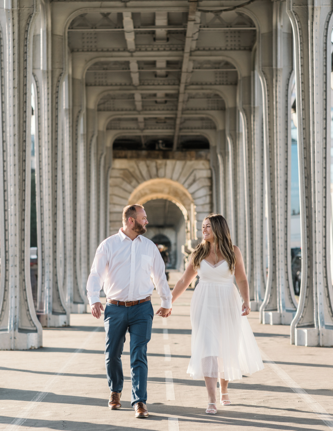 engaged couple walk hand in hand under bir hakeim bridge in paris