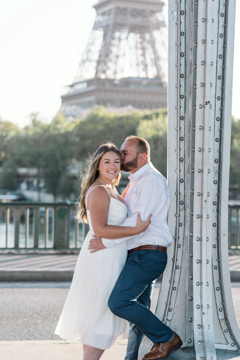 man kisses fiancee on cheek as she smiles with view of eiffel tower