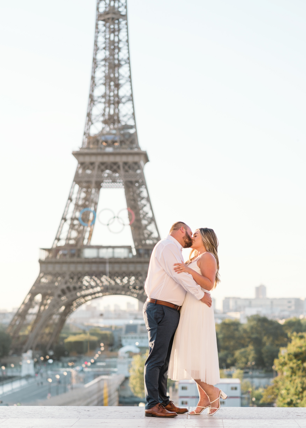 beautiful engaged couple kiss in front of eiffel tower in paris with olympic rings