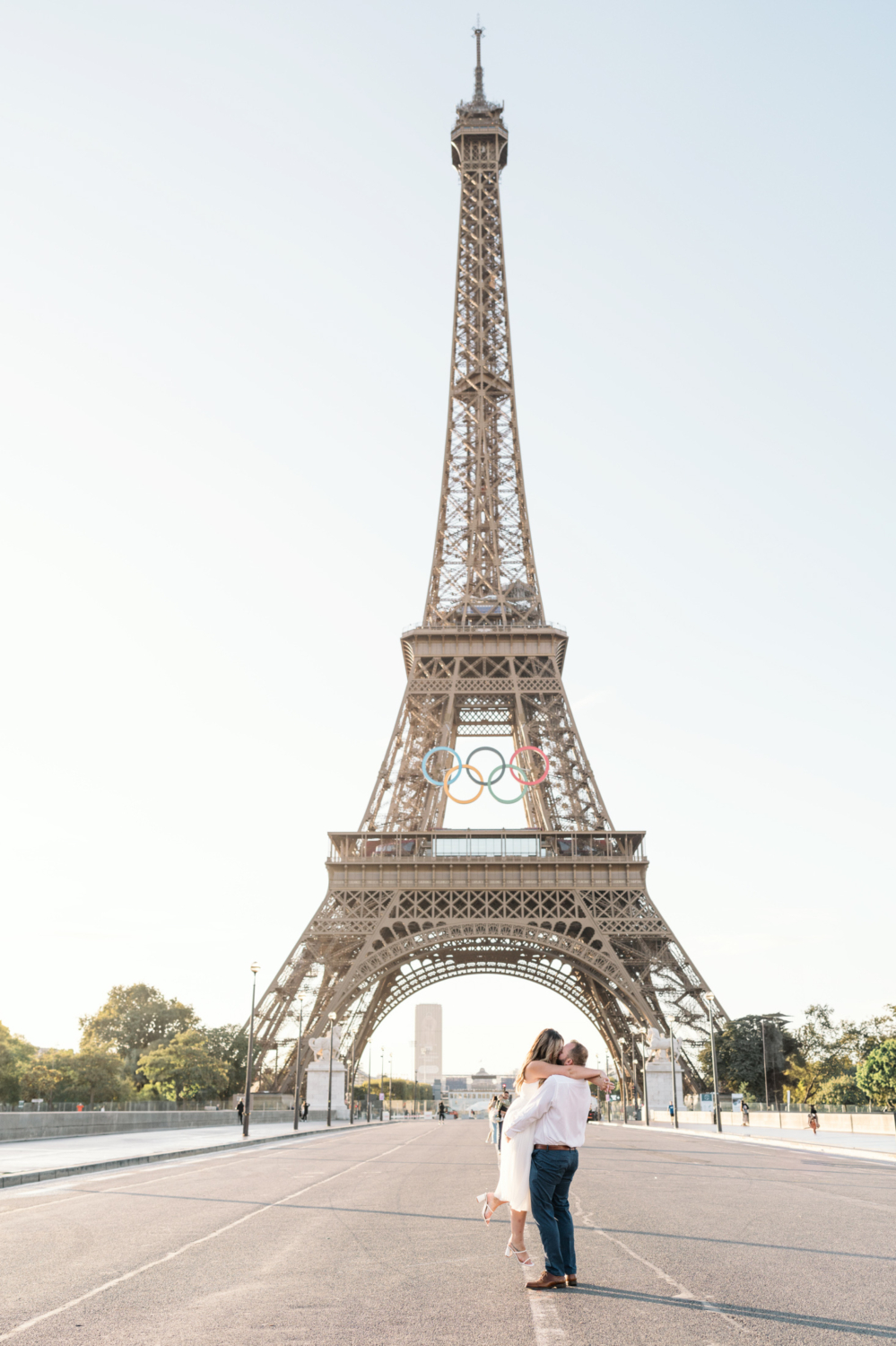 man lifts woman and kisses her with view of the eiffel tower in paris france with olympic rings