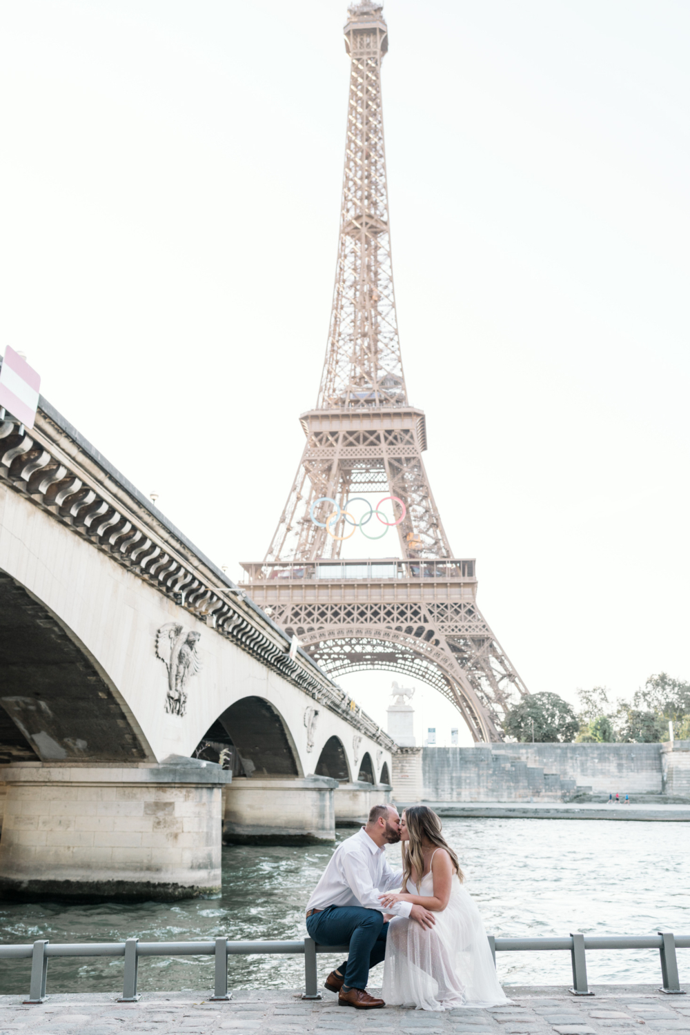 engaged couple kiss passionately while seated with view of the eiffel tower