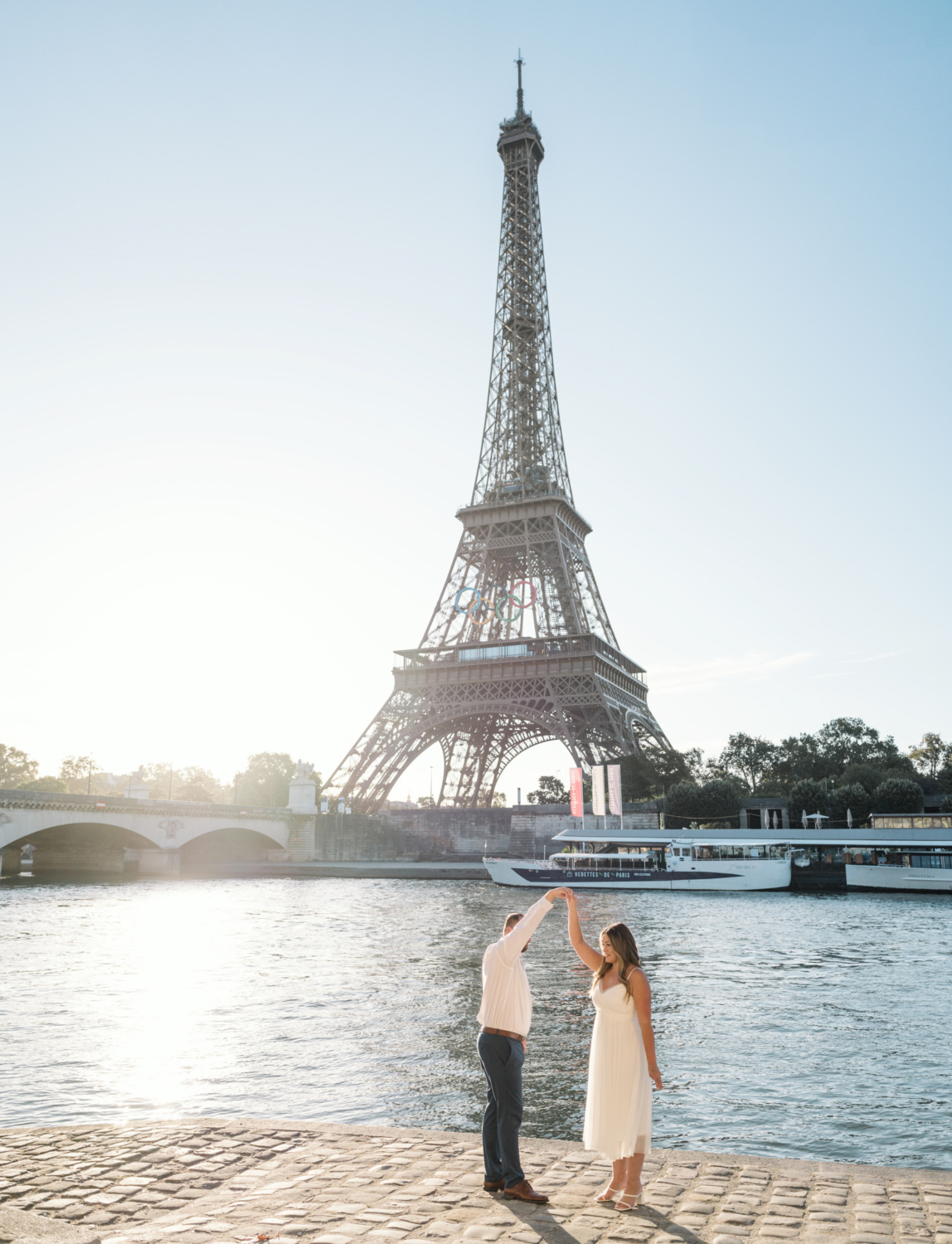 engaged couple dance next to the seine river in paris with view of eiffel tower