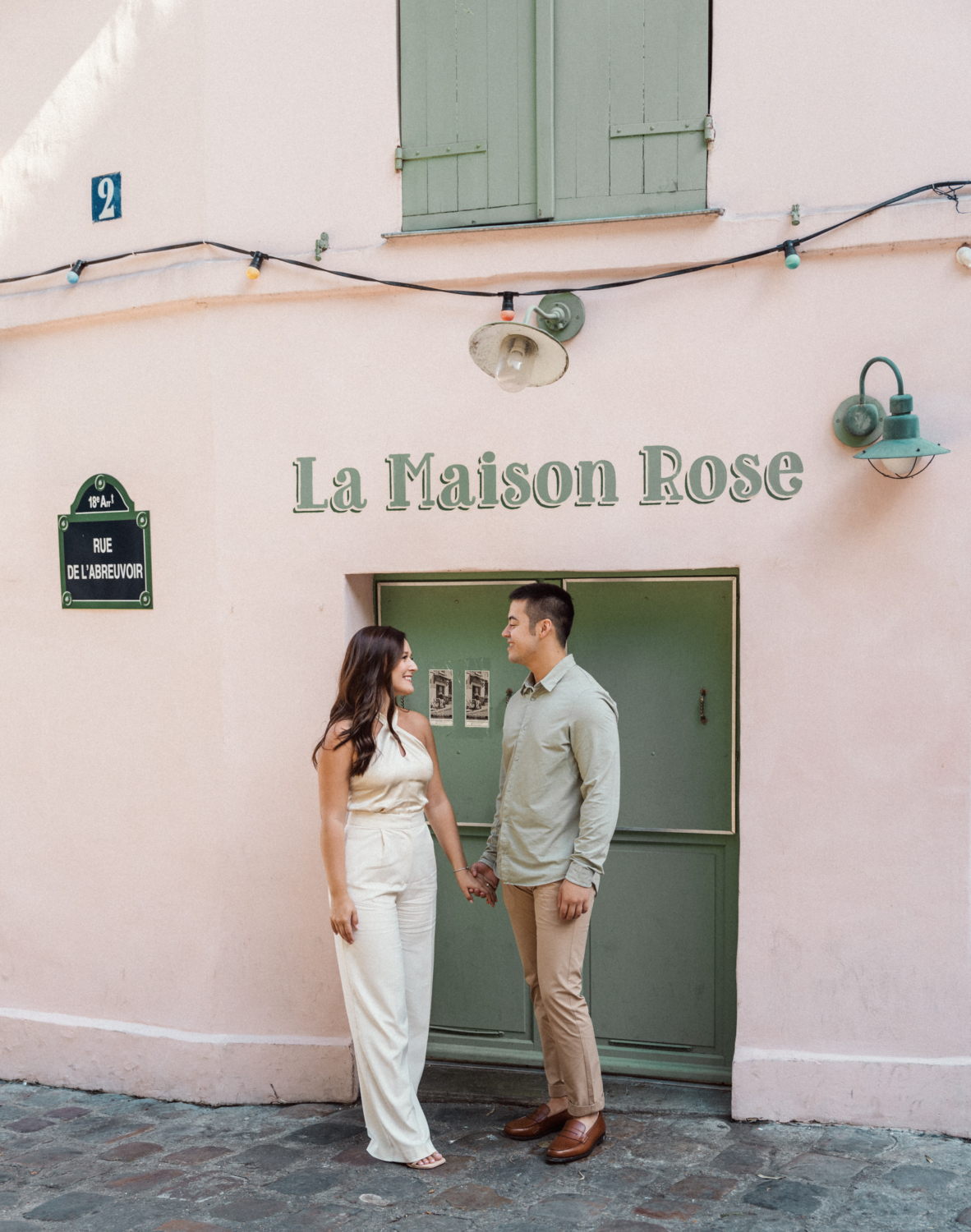 engaged couple pose in front of pink restaurant in montmartre paris