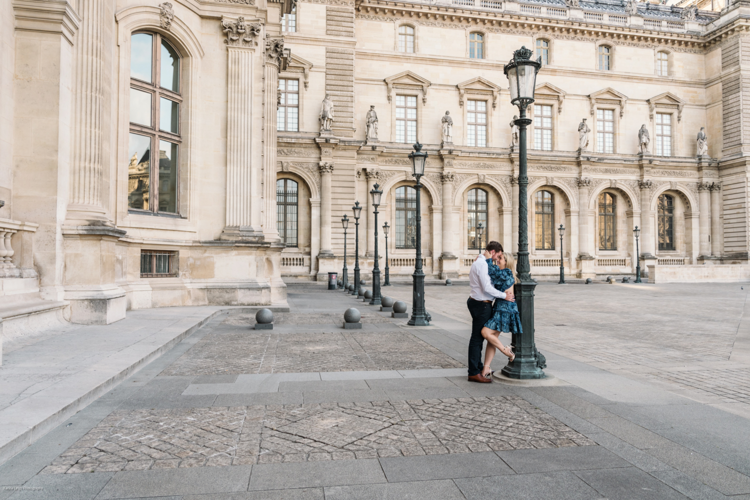 young newly engaged couple embrace in the courtyard of the louvre museum in paris