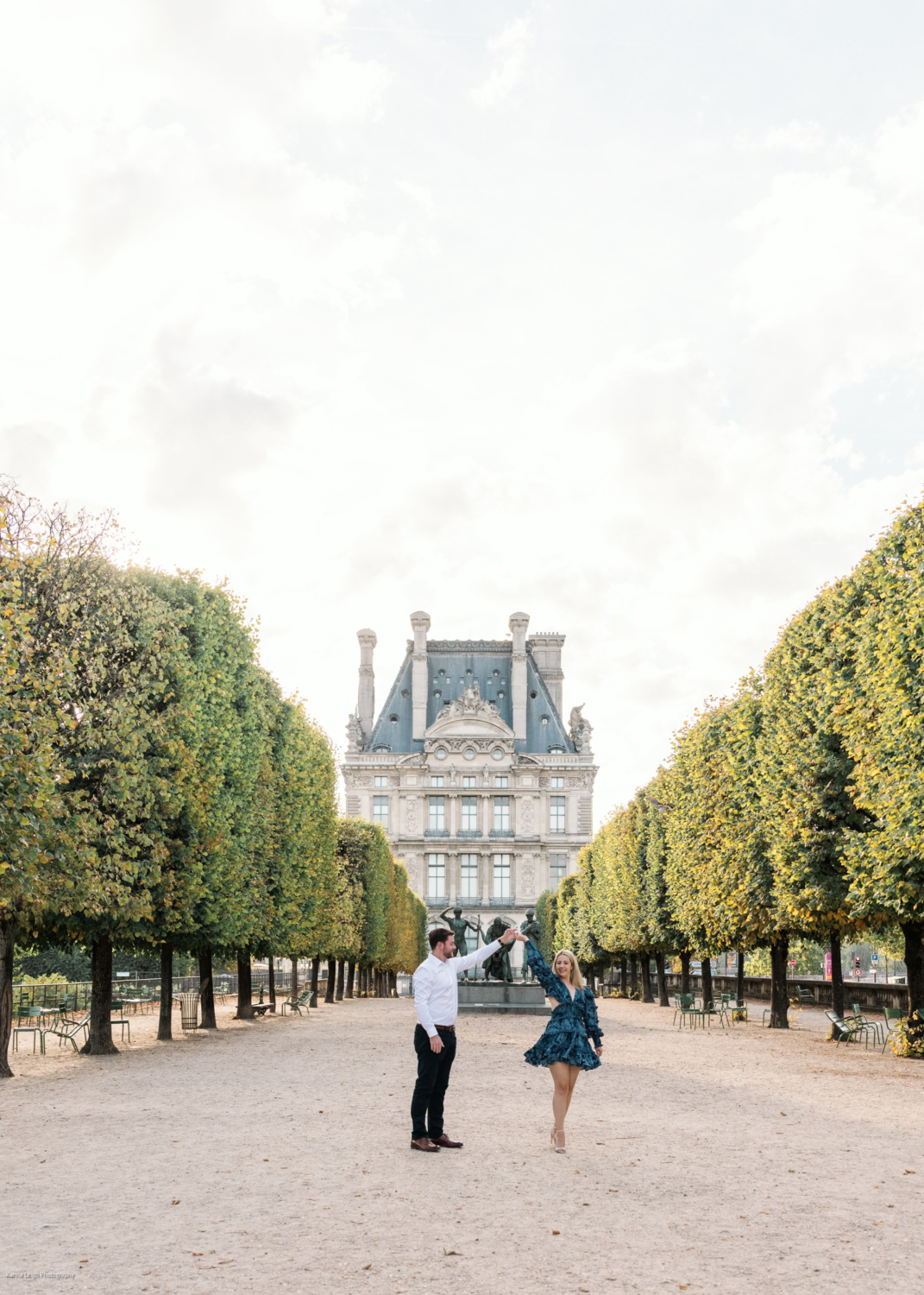 young newly engaged couple dance with a view of the louvre in paris during engagement photoshoot