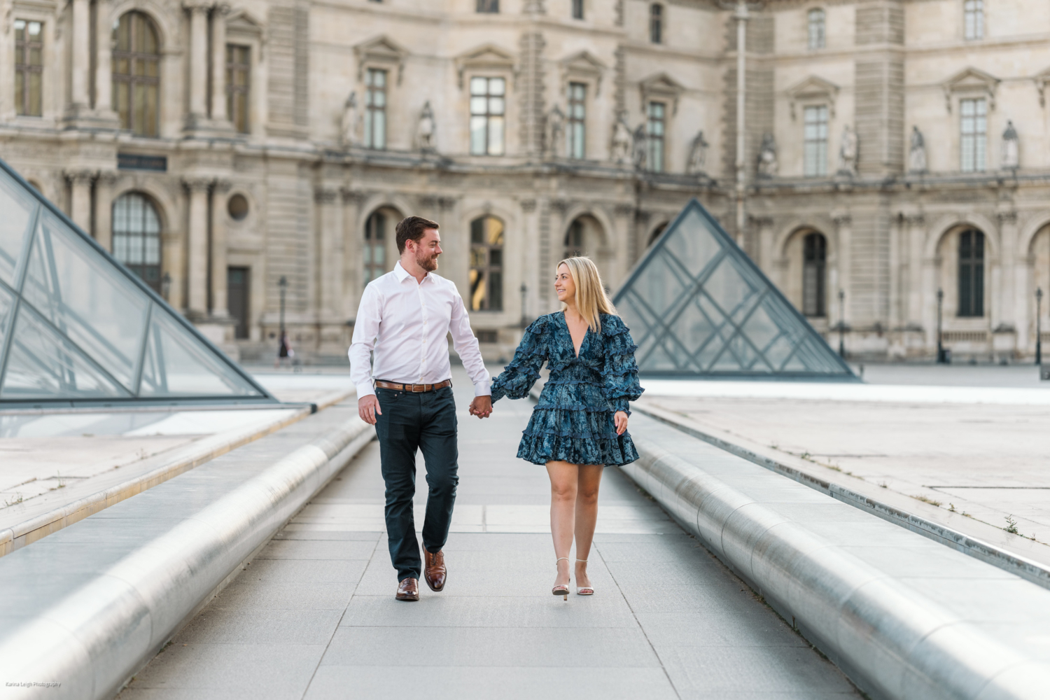 young newly engaged couple walk hand in hand at the louvre museum in paris