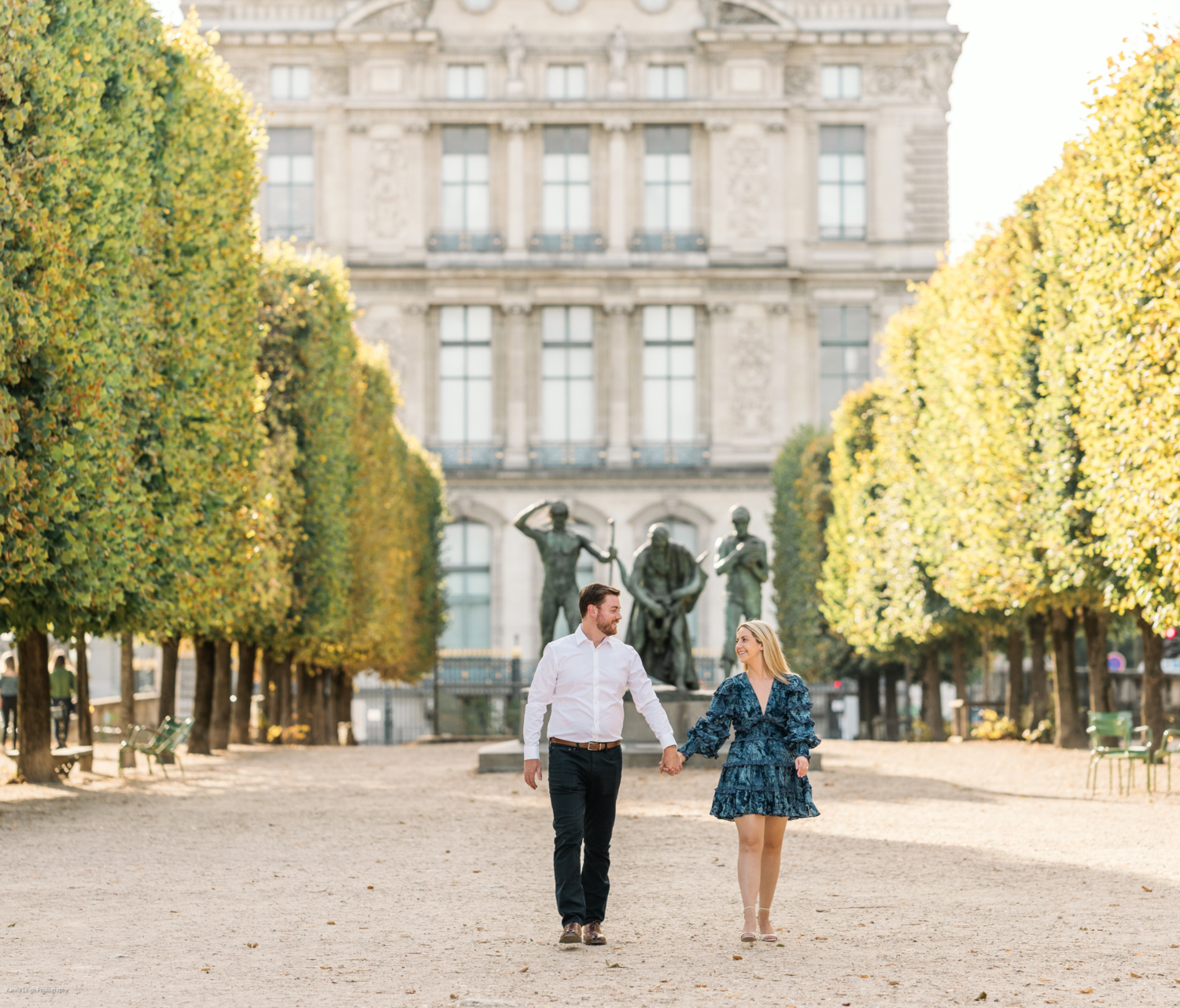 young newly engaged couple walk hand in hand with the louvre museum in background in paris