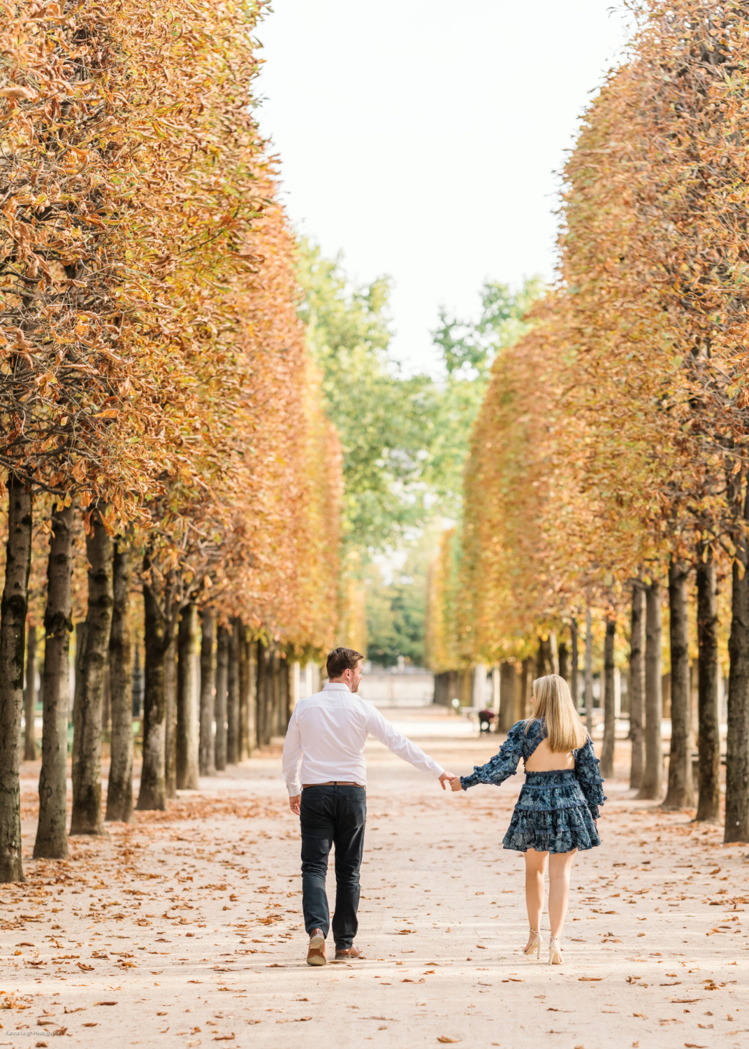 young newly engaged couple walk between colorful autumn trees in paris france