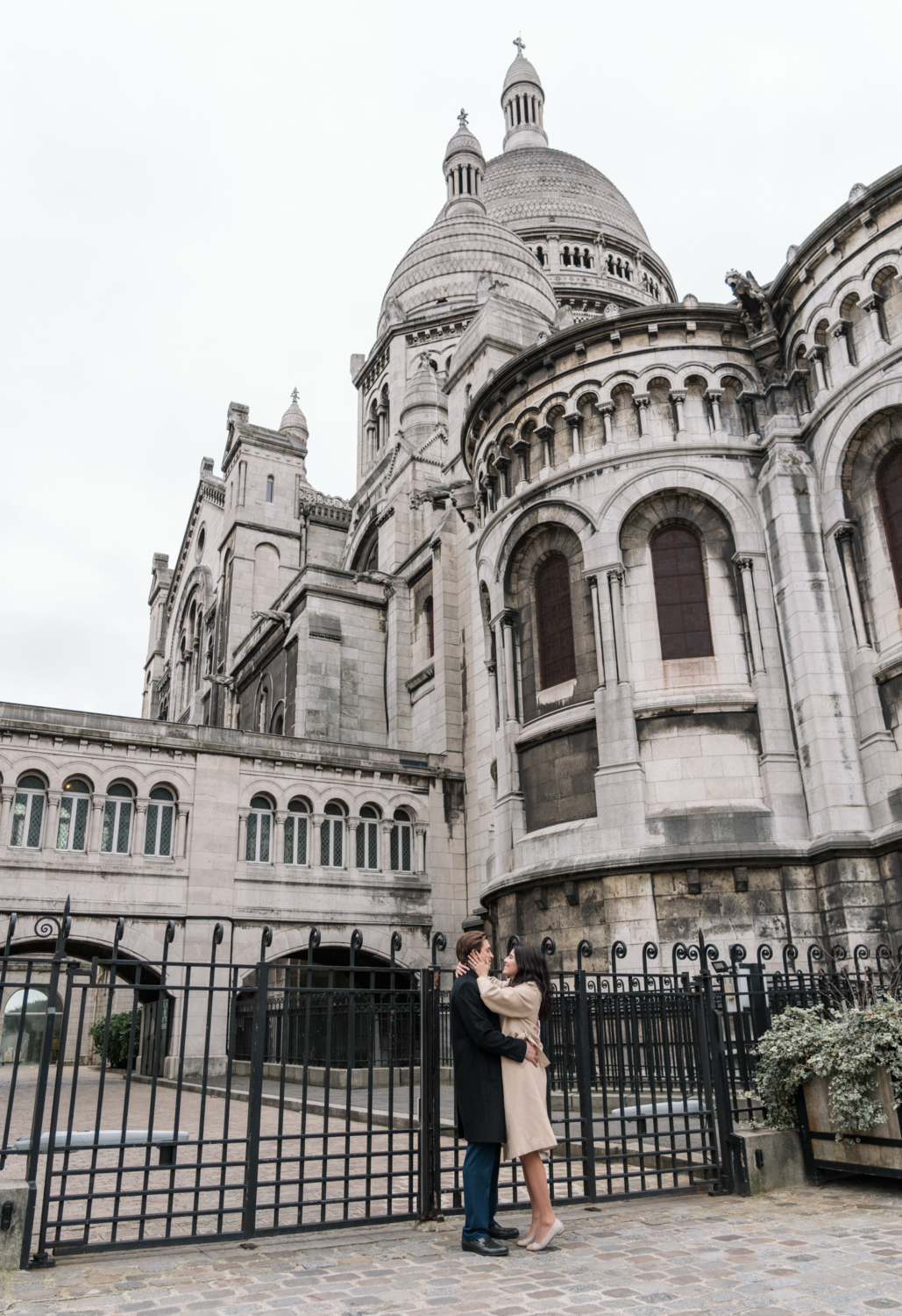 newly engaged couple embrace behind sacre coeur basilica in paris