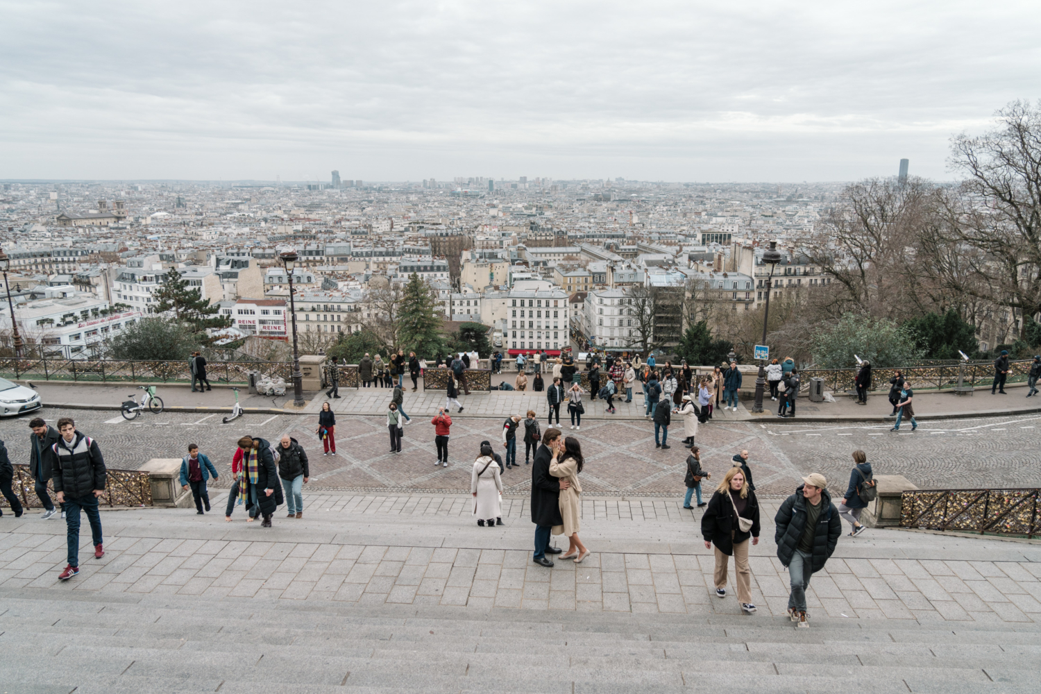 newly engaged couple kiss on the steps with view of paris at montmartre