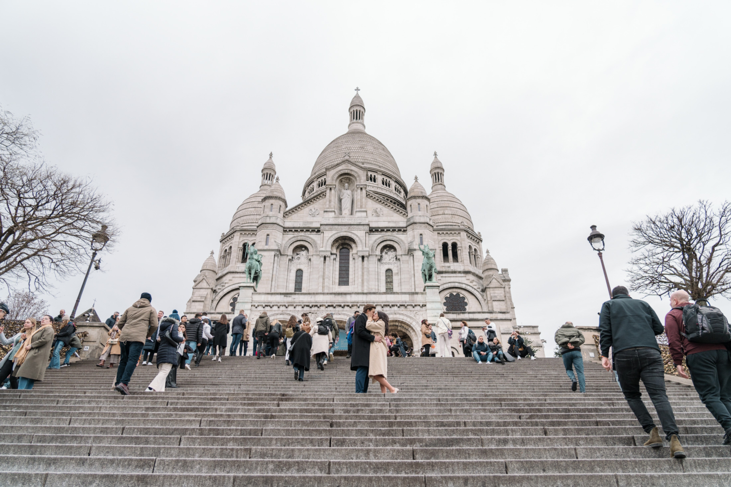 newly engaged couple kiss passionately on the stairs beneath sacre coeur basilica in paris france