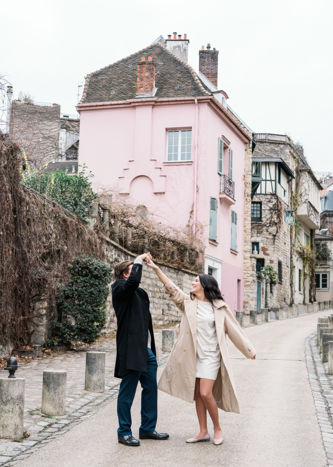 newly engaged couple dance on charming street with pink building in paris france