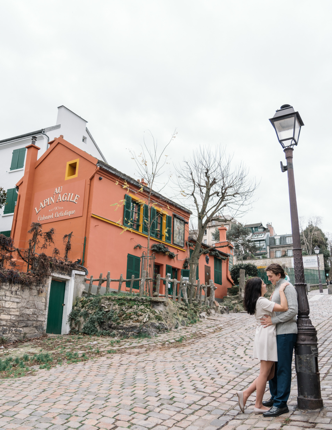 newly engaged couple embrace in front of charming orange building in montmartre paris france