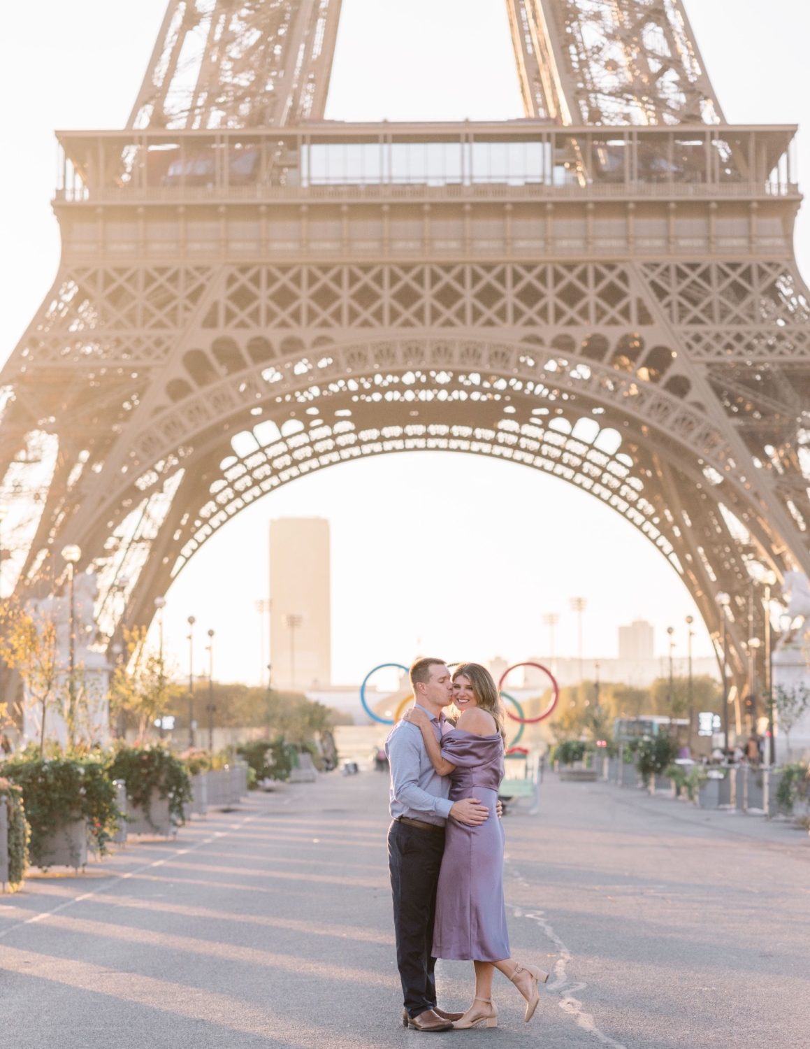 husband kisses wife on cheek with eiffel tower and olympic rings behind them