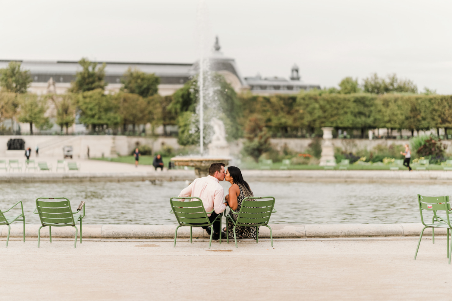 newly engaged couple kiss while sitting on chairs near the fountain in tuileries gardens paris france