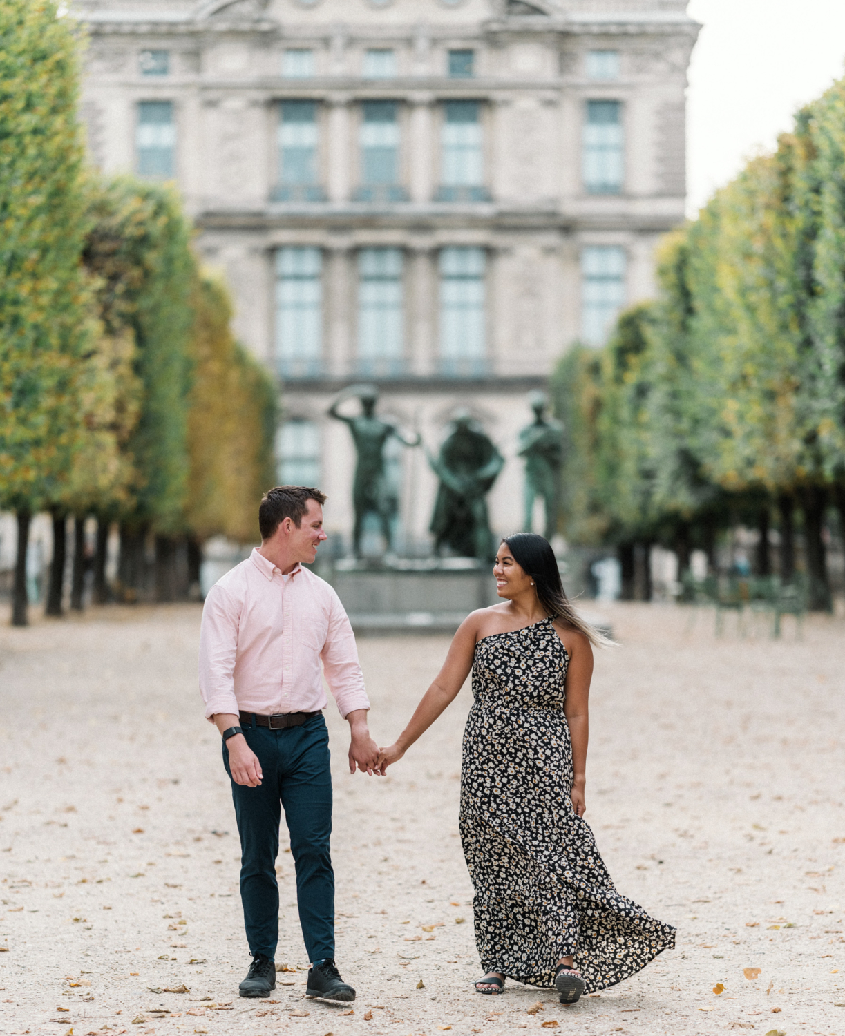 newly engaged couple smile and laugh as they walk through tuileries gardens in paris