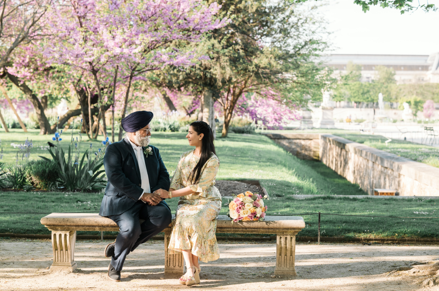 mature indian couple hold hands as they sit on bench in tuileries gardens paris