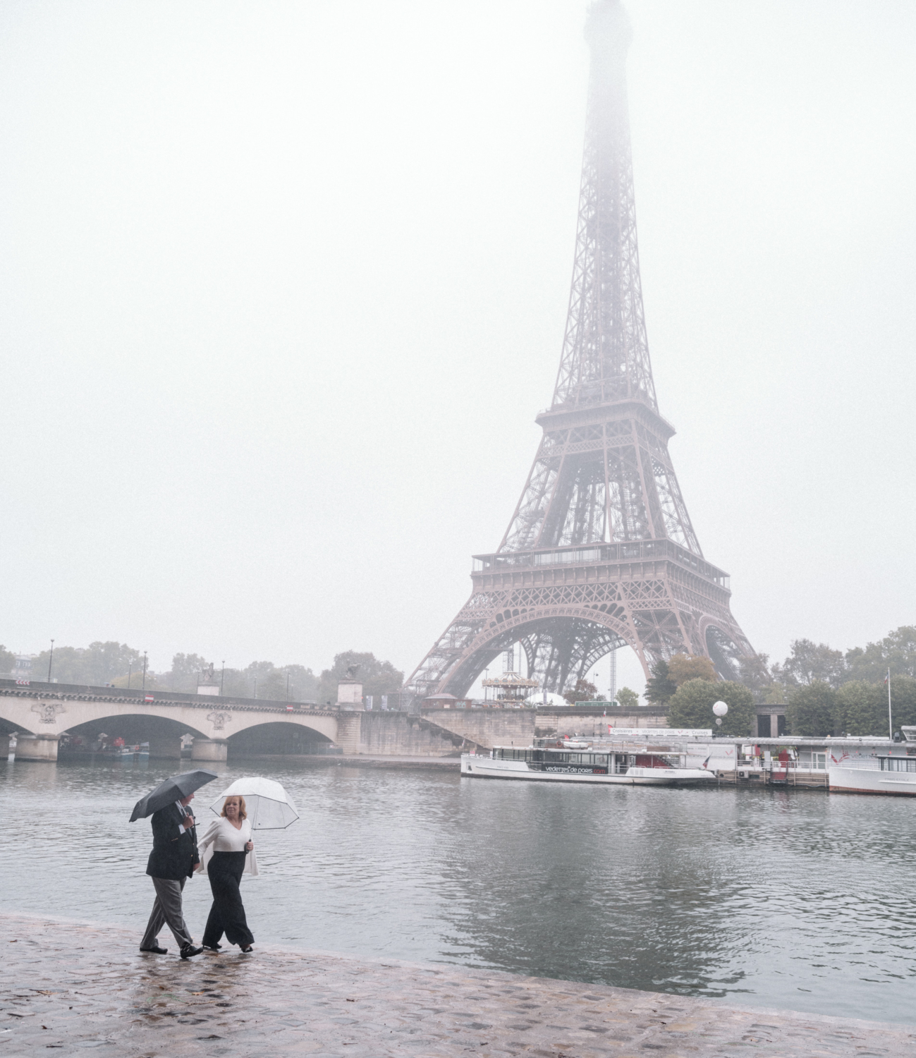 mature bride and groom walk in the pouring rain with view of the eiffel tower