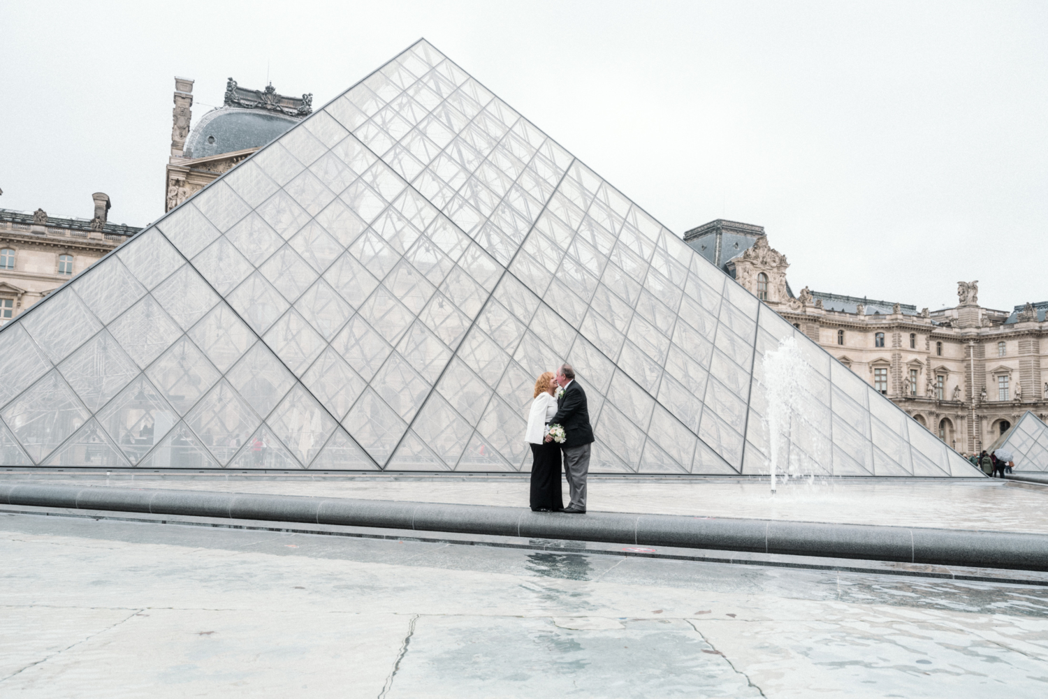 mature newlywed couple kiss at the pyramid of the louvre in paris