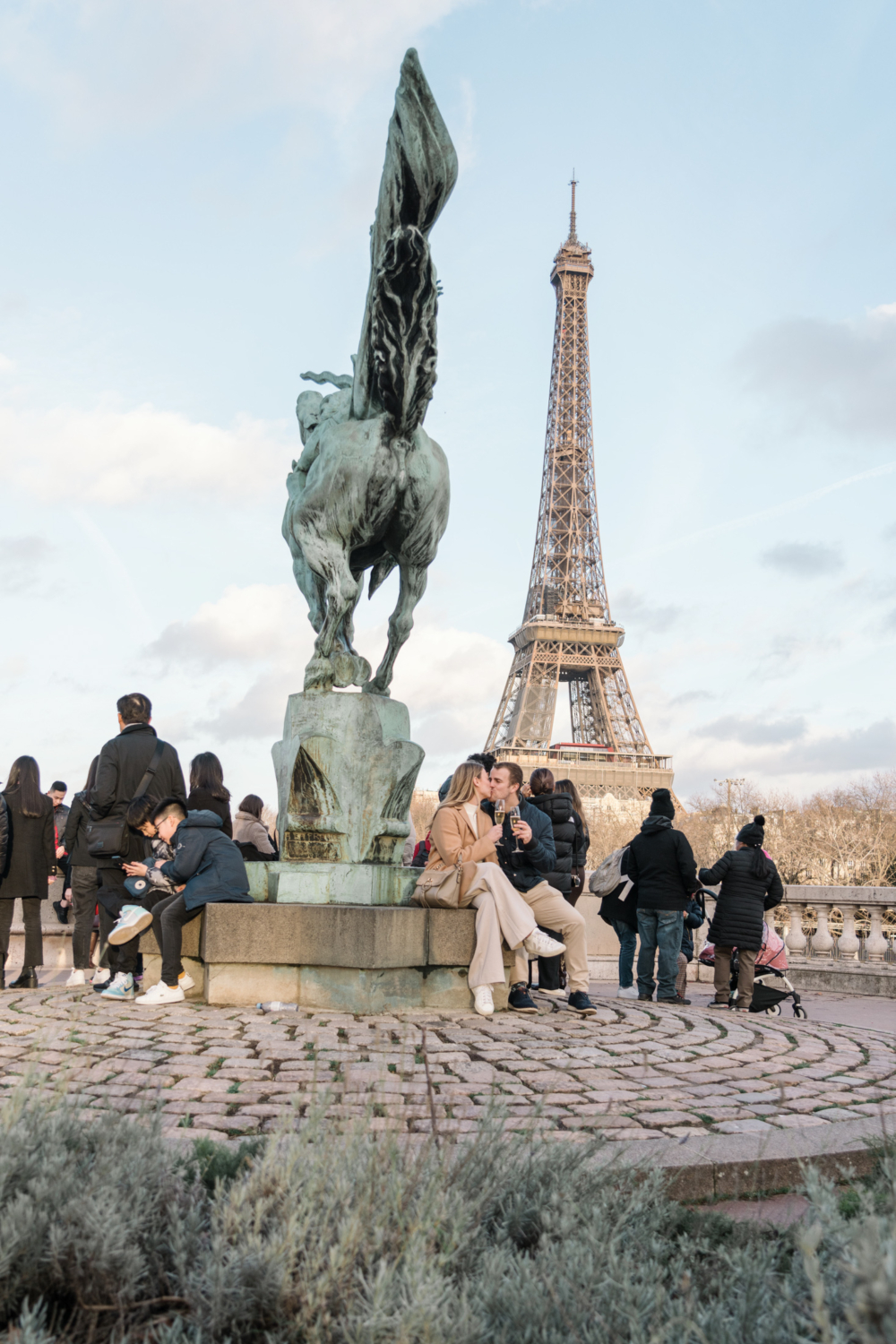 couple kiss and drink champagne next to statue with view of eiffel tower in paris